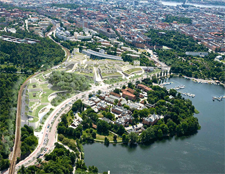 Flygfoto över byggnader belägna invid grönområde och vatten. Visar byggnadsklustrer och distrikt.